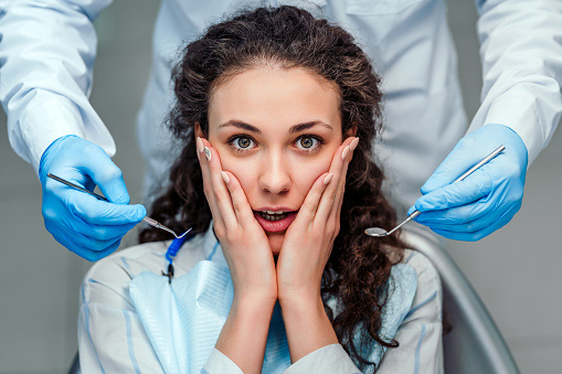 Patient with hands on face in front of doctor with dental tools at Peak Endodontics in Covington, WA